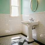 Small vintage bathroom interior showing high-contrast black and white penny tile flooring, crisp white subway wainscoting, and upper walls painted in a soft mint green.