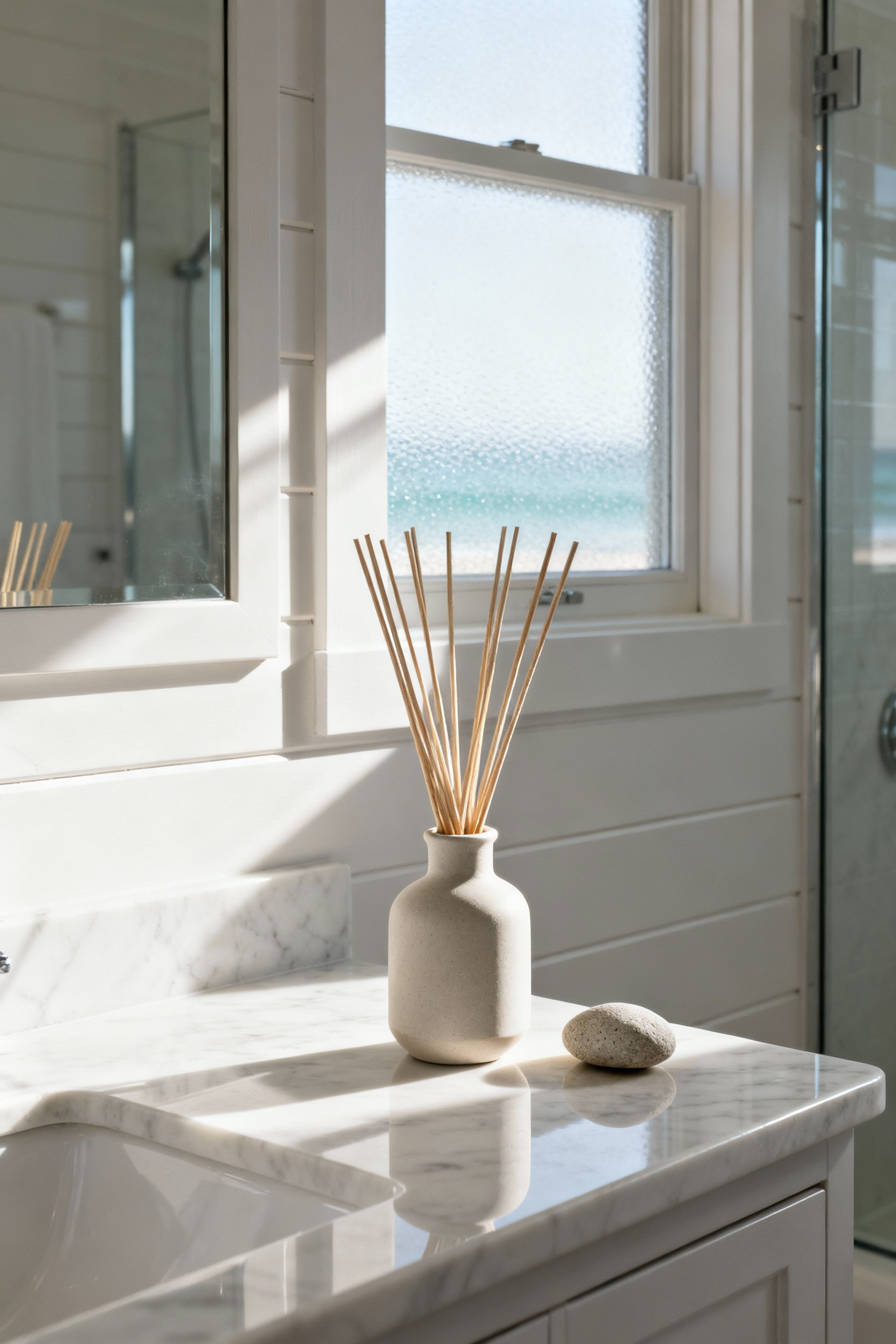 A serene coastal bathroom scene featuring a minimalist reed diffuser on a marble vanity, surrounded by natural elements. Soft light illuminates the space, creating a calm and inviting atmosphere with subtle oceanic scents.